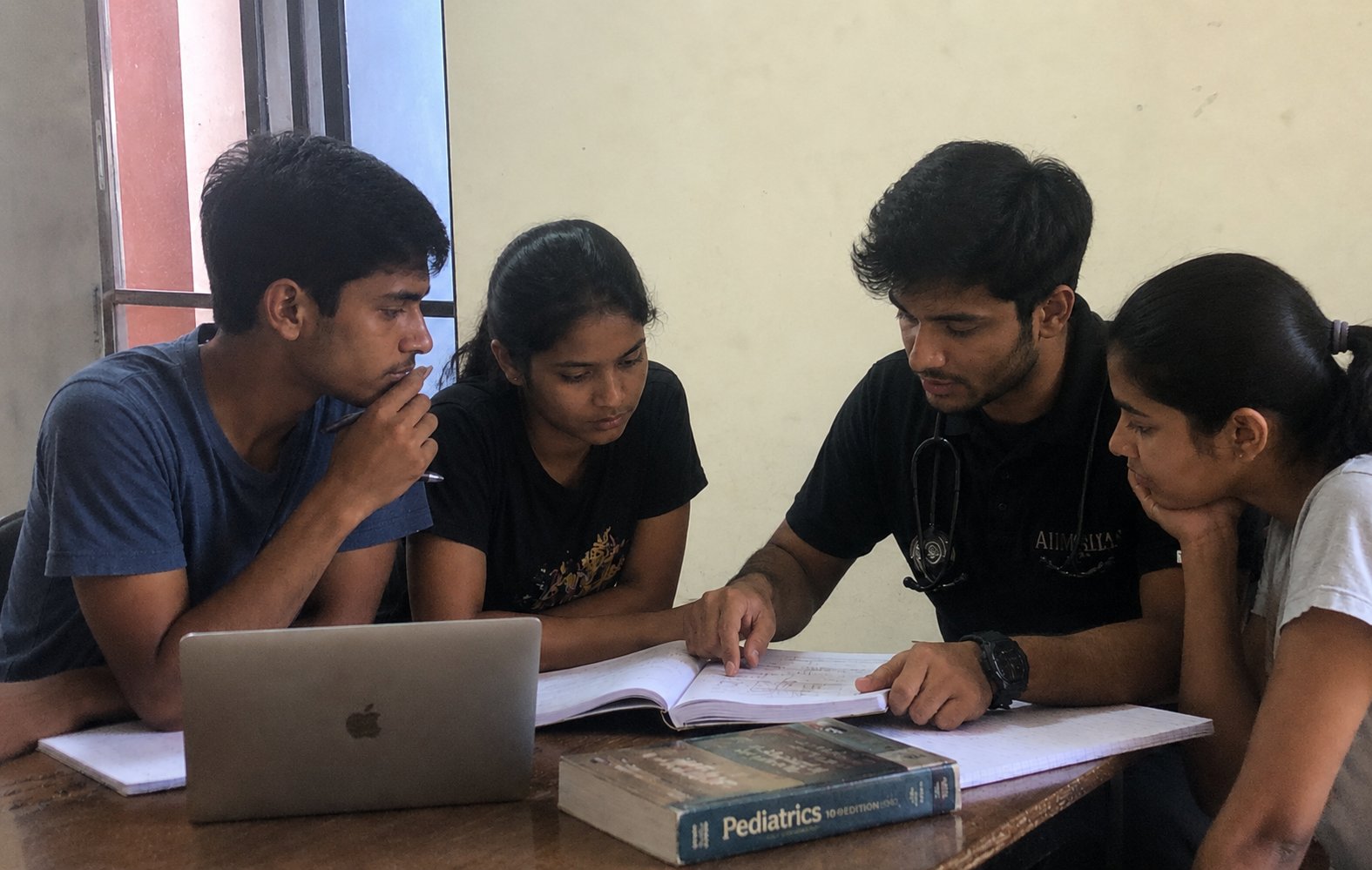 A medical student mentor going through a notebook with three NEET aspirants at a table